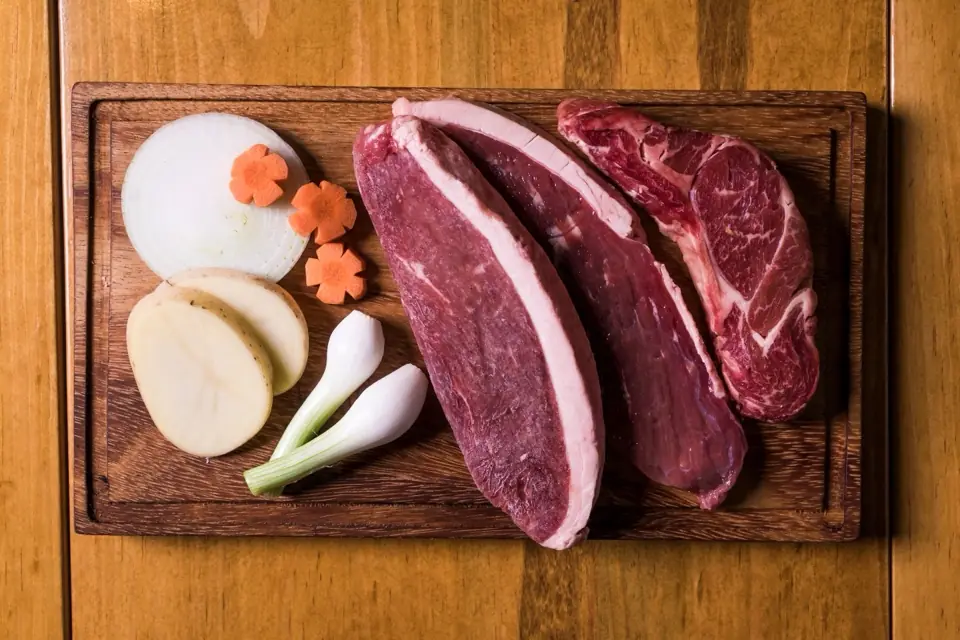 Fresh cuts of red meat on a wooden board with onion and spring onions