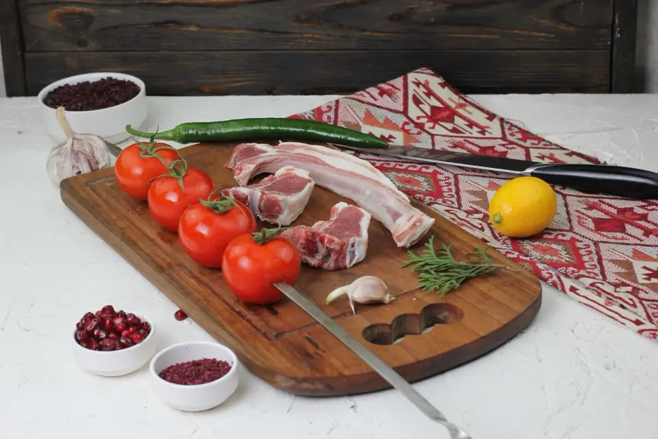Raw lamb chops on a board with tomatoes, garlic, pomegranate and a knife