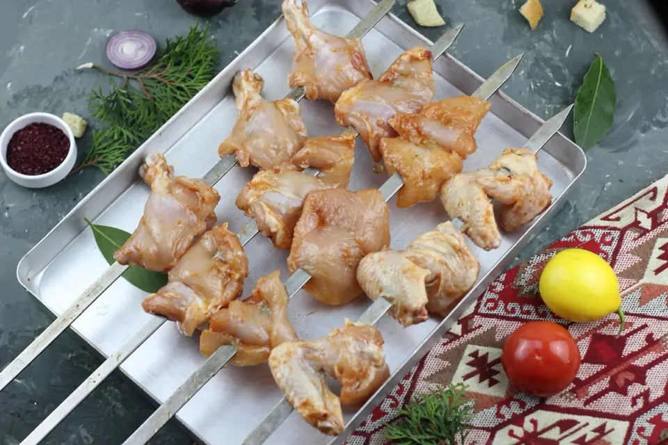 Marinated chicken pieces on steel skewers on a tray, ready for the grill