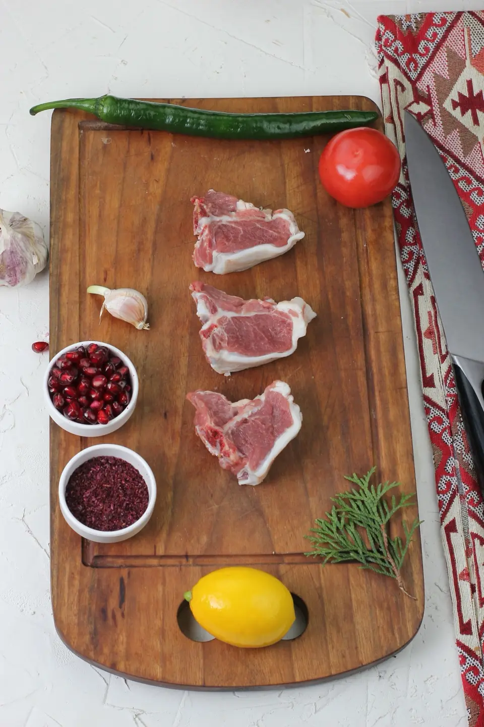 Raw mutton pieces on a board, seen from above, with herbs, spices and vegetables